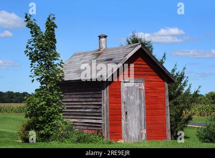 Rouge, en bois, fumoir se trouve sur la ferme dans le Wisconsin. Le tuyau de fumée dépasse du toit. Le bois est usé et vieux. Banque D'Images