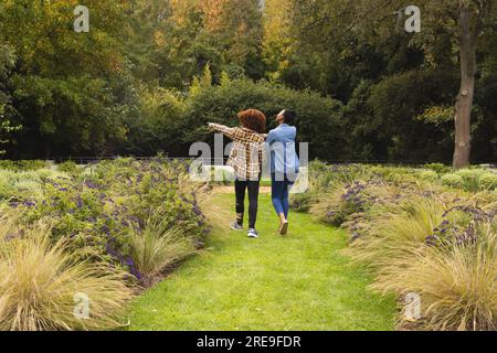 Vue arrière d'heureux couple diversifié tenant la main, marchant dans le jardin et pointant Banque D'Images