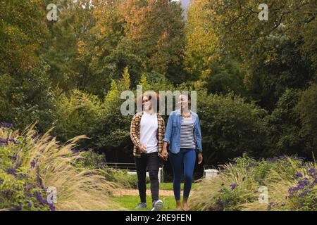 Heureux couple diversifié tenant la main, marchant dans le jardin et parlant Banque D'Images