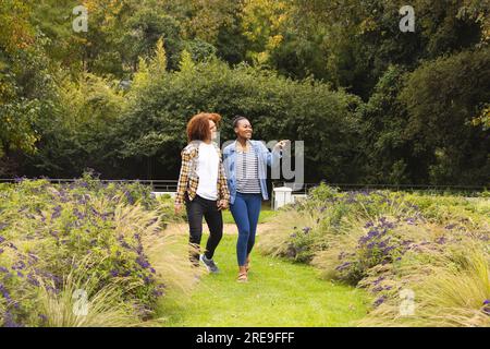 Heureux couple diversifié tenant la main, marchant dans le jardin et pointant Banque D'Images