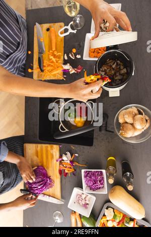 Section médiane de divers couples préparant le repas, hachant les légumes et compostant les déchets dans la cuisine Banque D'Images