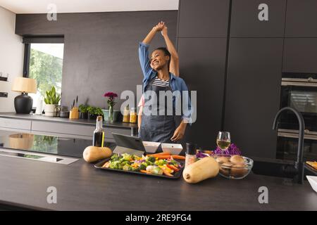 Heureux couple diversifié dans des tabliers préparant le repas en s'amusant à danser dans la cuisine Banque D'Images