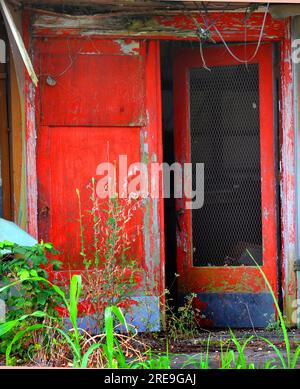 Un magasin délabré et fermé a ses portes rouges ouvertes. Les portes rouges sont fissurées et la peinture s'écaille. Des planches pourries pendent du haut. Banque D'Images