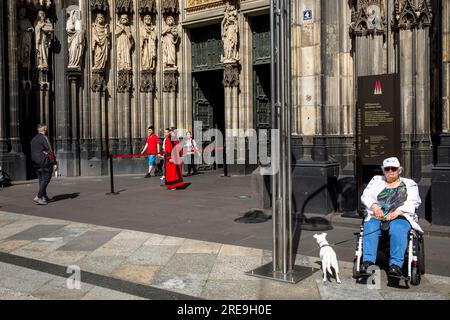 Femme en fauteuil roulant avec chien attendant devant le portail de la cathédrale, Cologne, Allemagne. Frau im Rollstuhl mit Hund wartet vor dem Domportal, Koeln, D. Banque D'Images