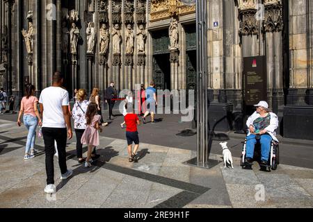 Femme en fauteuil roulant avec chien attendant devant le portail de la cathédrale, Cologne, Allemagne. Frau im Rollstuhl mit Hund wartet vor dem Domportal, Koeln, D. Banque D'Images