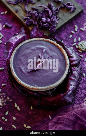 gros plan d'un bol en céramique rustique avec un peu de soupe au chou rouge saupoudré de chou rouge cru haché, sur une surface texturée violette Banque D'Images