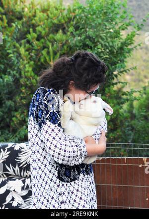 Jeune femme câlinera son grand lapin géant flamand blanc. Elle est debout à l'extérieur et a sur une chemise imprimée et des lunettes. Banque D'Images