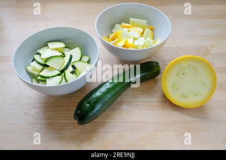 Courgettes vertes et jaunes, entières et hachées dans un bol, ingrédient pour divers plats de légumes sur une planche de cuisine en bois, concept de cuisine végétarienne, Banque D'Images