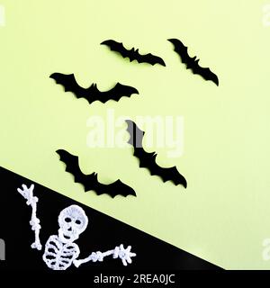 Composition de chauves-souris noires sur fond vert et squelette blanc tricoté sur fond noir. Concept Halloween. Banque D'Images