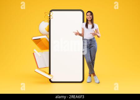 Jeune femme joyeuse pointant vers Big Phone sur fond jaune Banque D'Images