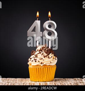 Cupcake d'anniversaire avec bougie numéro 48 - célébration sur fond sombre Banque D'Images