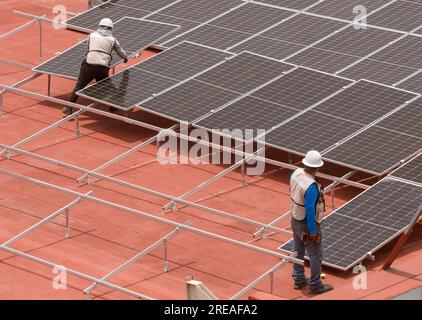 Ouvriers installant des panneaux solaires sur la terrasse de toit Banque D'Images