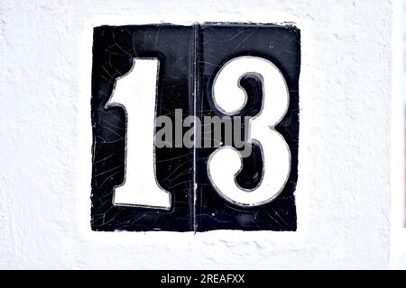 Grand numéro 13, treize, sur des carreaux noirs sur un mur blanc. Banque D'Images