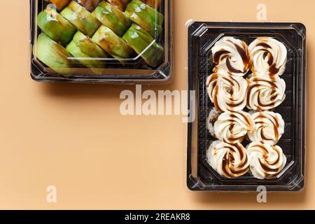 Ensemble de rouleaux de sushi dans des emballages en plastique à emporter sur un fond clair. Rouleaux avec saumon, crevettes, avocat, fromage à la crème, vue de dessus, espace pour le texte. Banque D'Images