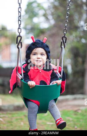 Petite fille de bébé portant un costume de coccinelle assis sur un balançoire d'enfant en bas âge. Concept Halloween. Banque D'Images