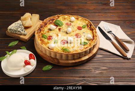 Délicieuse quiche au fromage mozzarella, tomates et basilic sur table en bois Banque D'Images