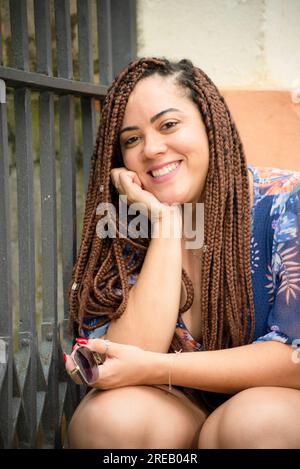 Portrait d'une jolie femme souriant avec des tresses dans les cheveux et la main sur son menton regardant la caméra. Pelourinho, Brésil. Banque D'Images