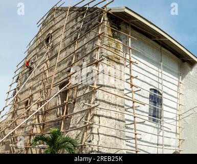 Île de Cebu, Philippines-27 janvier 2023 : utilisant des poteaux de bambou comme échafaudage et portant des tongs sur ses pieds, l'ouvrier applique de la peinture blanche t Banque D'Images