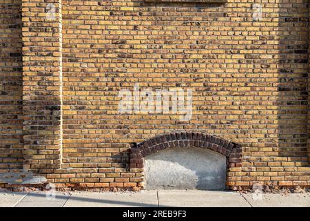 Fond de texture plein cadre d'un joli vieux mur de briques de couleur jaune et marron marbré, avec vue sur une fenêtre de sous-sol arquée fermée Banque D'Images