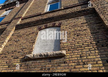 Vue plein cadre à faible angle d'un joli vieux mur de briques de couleur jaune et marron marbré, avec vue sur une fenêtre arquée scellée Banque D'Images