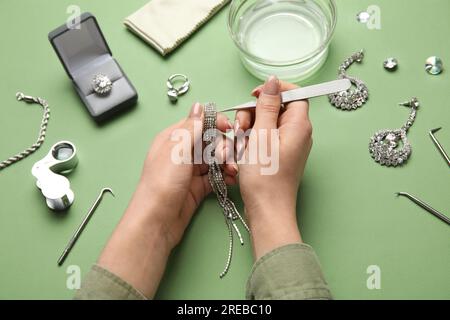 Femme nettoyant de beaux bijoux sur fond vert, gros plan Banque D'Images