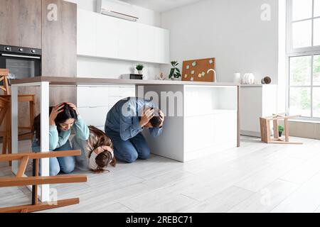 Famille effrayée se cachant sous la table à manger pendant le tremblement de terre dans la cuisine Banque D'Images