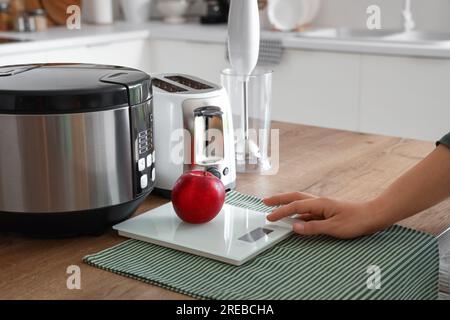 Femme mesurant la pomme sur une balance dans une cuisine moderne Banque D'Images