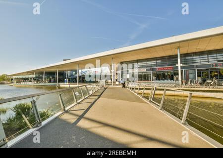 un quai de bateau avec des gens marchant sur la passerelle et en arrière-plan est un bâtiment qui ressemble à un centre commercial Banque D'Images