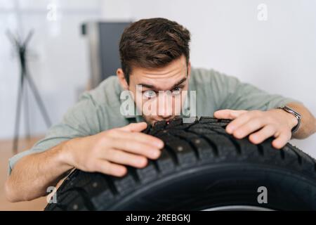 Portrait de drôle jeune homme client examinant la marque et les caractéristiques du produit tout en achetant de nouveaux pneus dans le département automobile de la concession. Banque D'Images