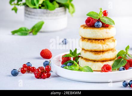 Crêpes épaisses au fromage cottage avec des myrtilles, des framboises et des groseilles rouges, décorées avec de la menthe sur une assiette blanche, délicieux petit déjeuner. Table grise Banque D'Images