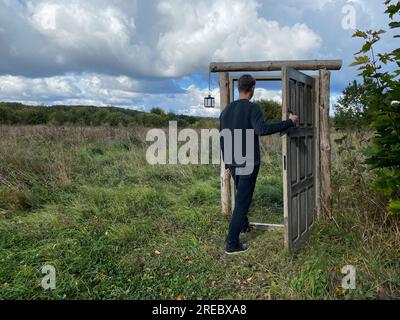 Homme passant par le vieux portail mystère dans le champ ouvert. Personne et la porte qui mène à nulle part. Concept de trouver une issue, existence d'une autre Banque D'Images