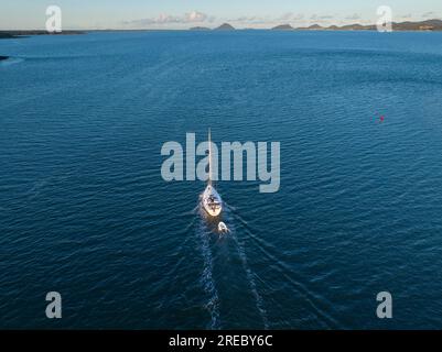 Un yacht solitaire remorquant un petit canot sur un large océan bleu à Soldiers point en Nouvelle-Galles du Sud, en Australie Banque D'Images