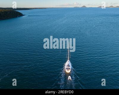 Un yacht solitaire remorquant un petit canot sur un large océan bleu à Soldiers point en Nouvelle-Galles du Sud, en Australie Banque D'Images