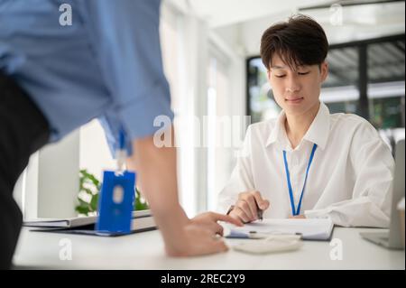 Un jeune travailleur de bureau asiatique intelligent se concentre sur l'examen de documents et de travailler sur un projet avec une collègue féminine au bureau. Banque D'Images