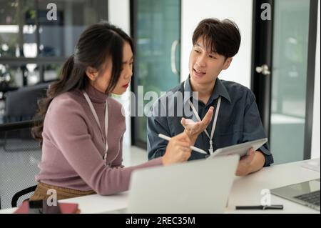 Deux employés de bureau asiatiques professionnels discutent du travail, brainstorming, partagent leurs idées et travaillent ensemble sur un projet au bureau. Banque D'Images