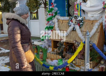 femme debout dans la rue en hiver près de la scène de la nativité en bois Banque D'Images