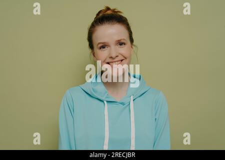 Séduisante adolescente en sweat à capuche urbain, cheveux en chignon, souriant avec gentillesse, exprimant des émotions positives en studio. Banque D'Images