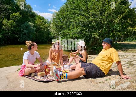 Pique-nique au bord du Doubs et du Canal Charles Quint à Dole (nord-est de la France) : groupe d'amis déjeunant au bord de l'eau en été, avec casquettes Banque D'Images