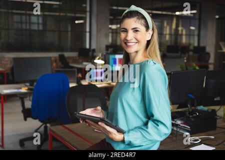 Portrait de femme biracial tenant une tablette numérique souriant au bureau Banque D'Images