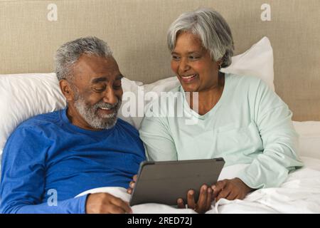 Heureux couple biracial senior couché dans le lit utilisant tablette à la maison Banque D'Images