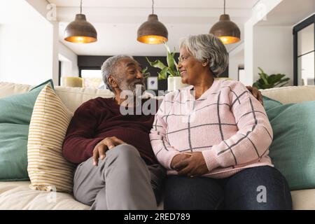Heureux couple biracial senior assis sur le canapé et souriant les uns aux autres à la maison Banque D'Images