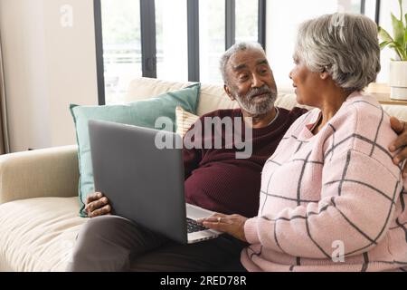 Heureux couple biracial senior assis sur le canapé et utilisant un ordinateur portable à la maison Banque D'Images