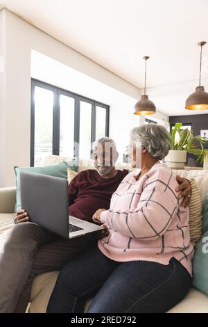 Heureux couple biracial senior assis sur le canapé et en utilisant un ordinateur portable à la maison, espace de copie Banque D'Images