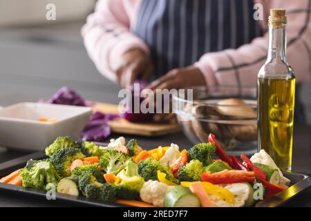 Femme biraciale senior portant un tablier et coupant du chou sur la table avec des légumes dans la cuisine à la maison Banque D'Images