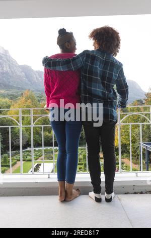 Vue arrière d'heureux couple diversifié sur le balcon embrassant et admirant la vue à la maison Banque D'Images