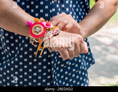 Frère main portant ou attaché rakhi à l'occasion du festival Raksha bandhan en Inde. mise au point sélective sur la main et flou d'arrière-plan. Banque D'Images