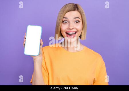 Portrait de fille impressionnée habillé des vêtements élégants présentant l'écran de smartphone espace vide regardant isolé sur fond de couleur violette Banque D'Images