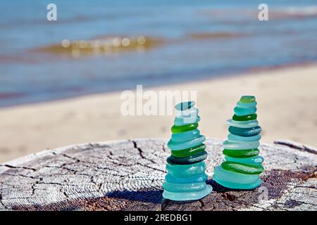 Deux pyramides zen de pierres de verre bleu et vert sur la surface en bois sur fond de vagues de la mer côtière Banque D'Images