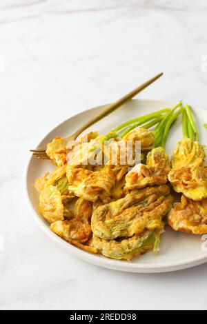 Fleurs de courgettes frites dans la pâte, assiette avec des fleurs de courgettes sur fond de marbre Banque D'Images