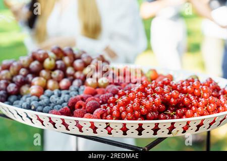 Un plat avec une variété de baies d'été, groseilles rouges, framboises, bleuets, groseilles, raisins lors d'un événement en plein air en été Banque D'Images